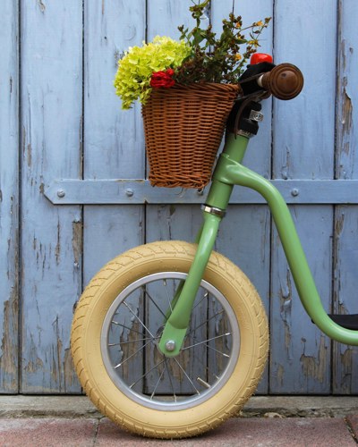 Billedet viser fronten af en løbecykel fra Puky. Cyklen har en cykelkurv som er pyntet fint med blomster.