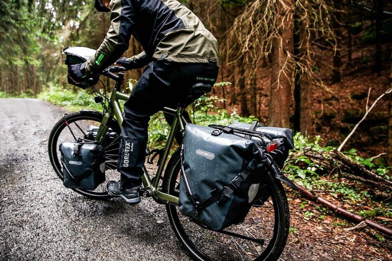 Billedet viser en person der cykler på en cykel, som har monteret adskillige Ortlieb cykeltasker på cyklen.