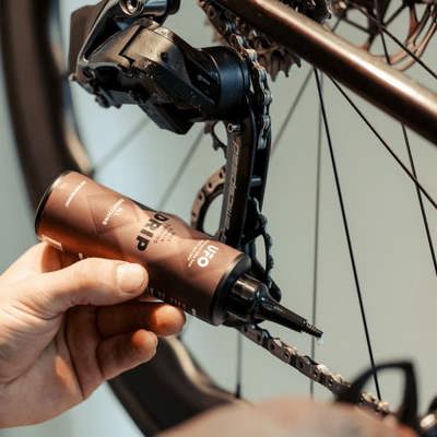 En hånd der illustrerer hvordan man kommer olie på en cykelkæde med en olie fra CeramicSpeed.