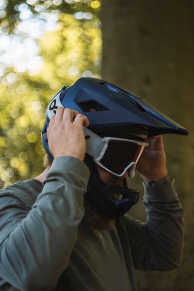Billedet viser en aktiv cyklist der er ved at tage et par googles udenover sin fullface hjelm.