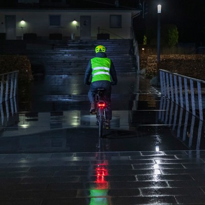 Billedet viser en cyklist der cykler i mørke. Cyklisten bærer en refleksvest og har cykellygter monteret. Billedet illustrerer hvor stor en forskel det kan gøre at bære lygter og reflekser.